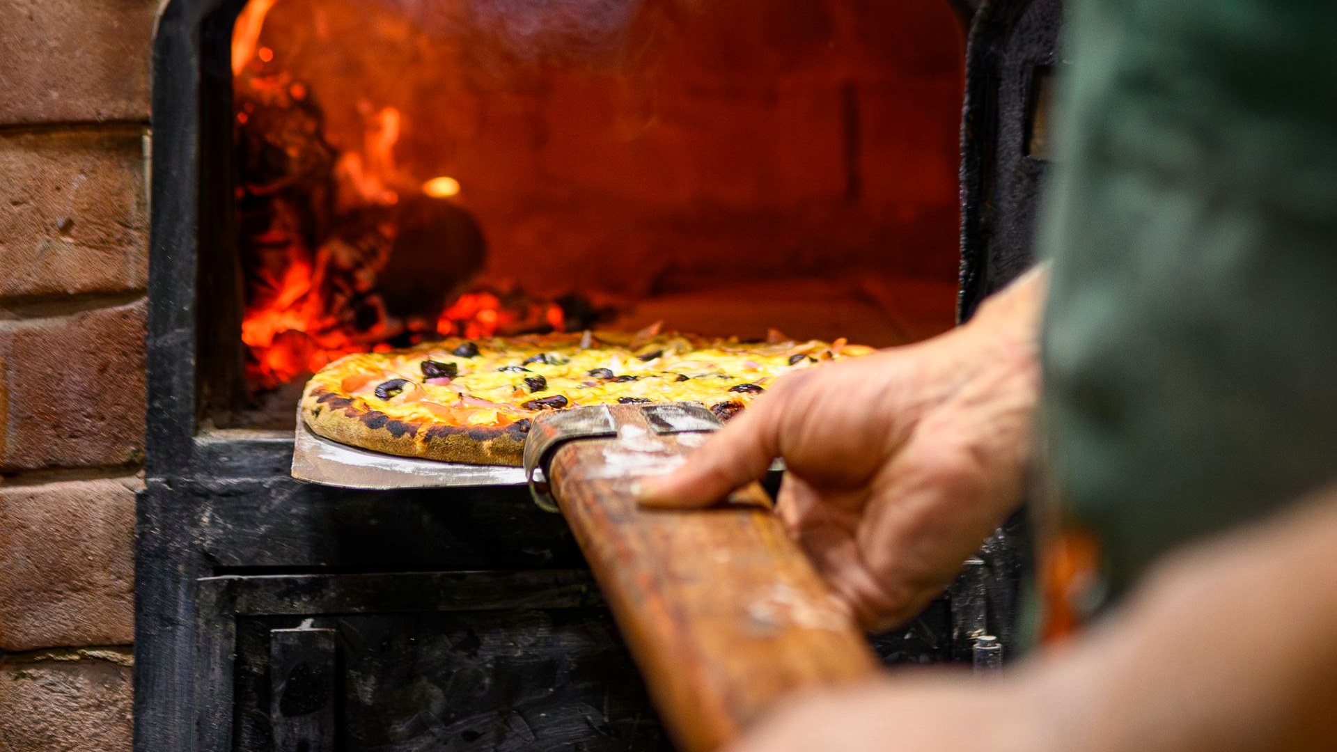 A wood-fired oven with a pizza going in